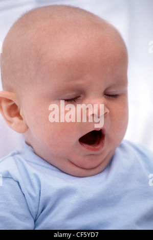 MMale baby, wearing a blue top, yawning with his eyes closed Stock Photo