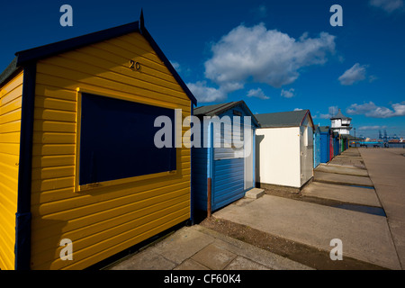 Freshly painted beach huts on the beach at Harwich. Felixstowe Docks can be seen in the background. Stock Photo