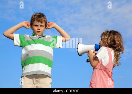 Children play on nature, girl shouts in loudspeaker, boy has closed ears. Stock Photo