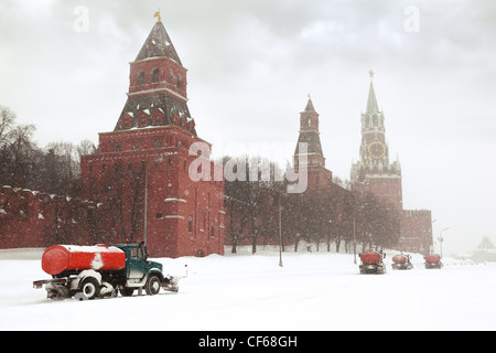 Four snow-remover trucks on road near Kremlin chiming clock Spasskaya Tower in Moscow Russia at wintertime during snowfall Stock Photo