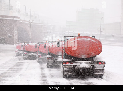 Column of five snow-remover trucks on the road in Moscow, Russia at wintertime during snowfall Stock Photo