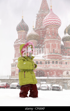 Little frozen girl standing in front of St. Basil's Cathedral in Moscow, Russia at wintertime during snowfall Stock Photo