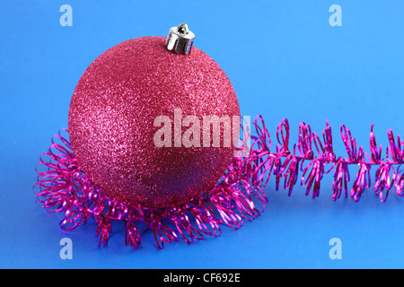One red Christmas tree ball surrounded by purple tinsel, isolated on blue. Stock Photo