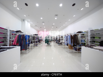 Inside the big shop, white hall with clothes on shelves and hanging outerwear Stock Photo