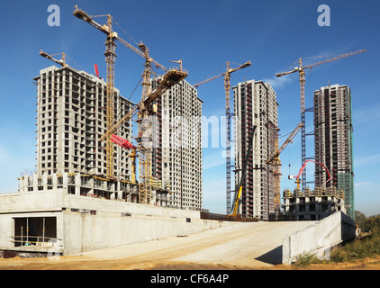 Four tall buildings under construction with cranes against a blue sky Stock Photo
