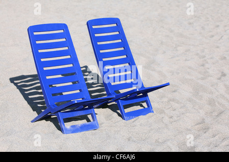 Two empty plastic chairs stand under sunbeams in  day-time on sand Stock Photo