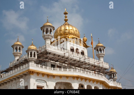 Scaffolding at upper levels of the Akal Takht in the Golden Temple, with a golden dome and some white clouds in the blue sky Stock Photo