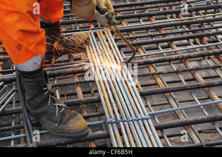 Worker legs in orange clothes weld metal grating by acetylene torch Stock Photo