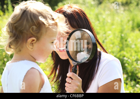 The little girl looks through a magnifying glass, which her mother holds Stock Photo