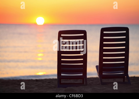 Two empty dark blue chairs stand on  beach in  evening with  view on marine sunset Stock Photo