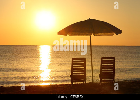 Two empty chairs stand on  beach under  opened umbrella with  view on marine sunset Stock Photo