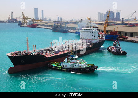 Two boats docked to industrial ship in port sail to sea at sunny day  in Abu Dhabi Stock Photo