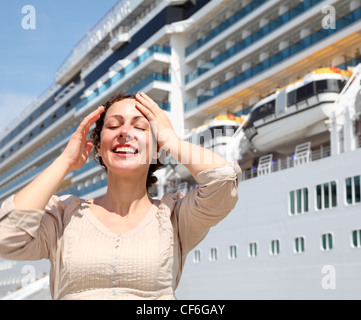 Smiling girl with closed eyes stands near the ship and smooths hair by hand Stock Photo