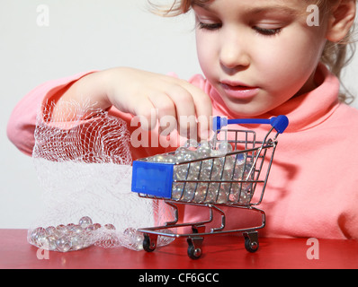 Cute little girl care play with toy shopping trolley filled by small balls Stock Photo
