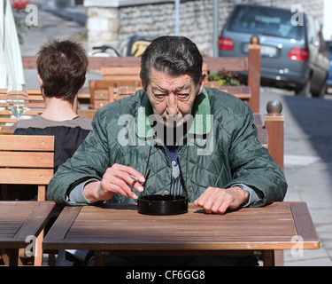 An Italian senior citizen sitting and smoking on a table outside a local wine bar. Spilimbergo, Italy. Stock Photo