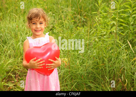 beautiful little girl in pink dress holding red balloon. Girl on nature