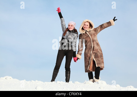 Two girls stand alongside  hold on  hands and lift free hand upwards Stock Photo