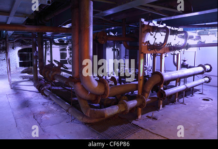 a lot of old pipes with valves located in a dirty basement Stock Photo