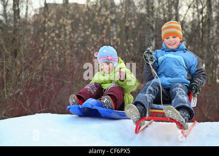 Girl and boy intend  drive from  hill in winter on sledges Stock Photo