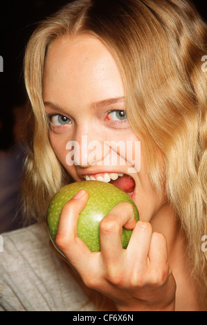 Backstage Milan Spring Summer Burberry Model Gemma Ward long wavy blonde hair wearing grey top biting into large green apple, Stock Photo
