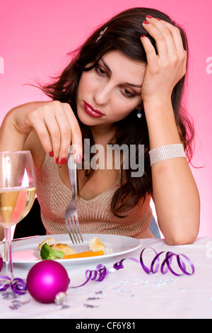 Female long brunette hair diamante hairclip wearing gold halterneck top sitting at table in front of plate small pieces of Stock Photo