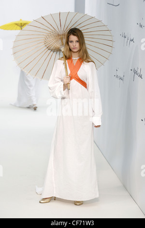 Agnes B Paris Ready to Wear Spring Summer Model long blonde hair wearing off white ankle length dress wide sleeves, orange Stock Photo