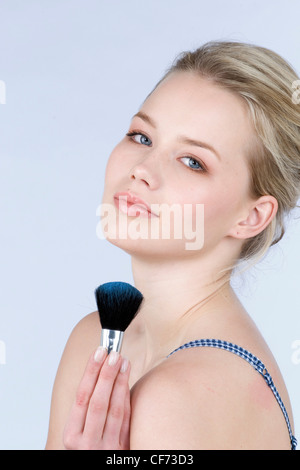 Female with soft brown eyeshadow, black mascara and soft pink glossy lips, holding a blusher brush with blue power on it Stock Photo