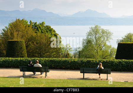 Three persons seated on two benches viewing Geneva lake. Stock Photo