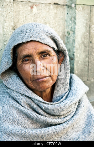 street portrait handsome indigenous beggar woman with expressive dark eyes crouched against stone wall in Centro district Oaxaca Stock Photo