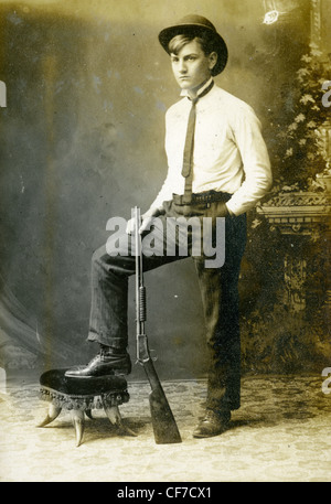Boy standing wearing suit and bowler hat during late 1800s or early 1900s 22 caliber pump action rifle guns gun weapons fashion Stock Photo
