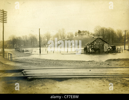 A blacksmith's stable is surrounded by water near railroad tracks in Indiana during the early 1900s. flooding black smith horses Stock Photo