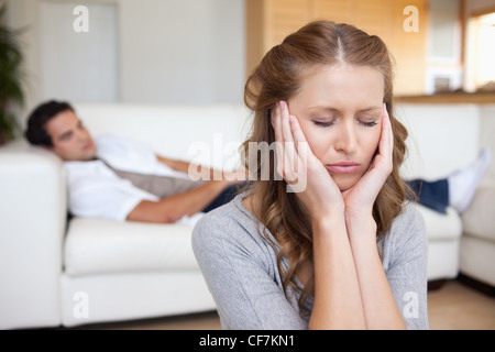 Woman having headache while man lying on sofa behind her Stock Photo
