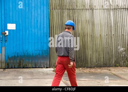 A workman wearing a hard hat walking in front of  warehouse Stock Photo