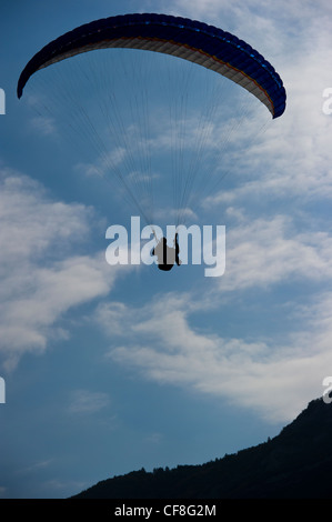 A silhouette of a paraglider coming into land against a blue sky with white clouds. Stock Photo