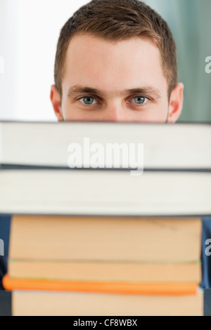 Close up of student hiding behind a stack of books Stock Photo