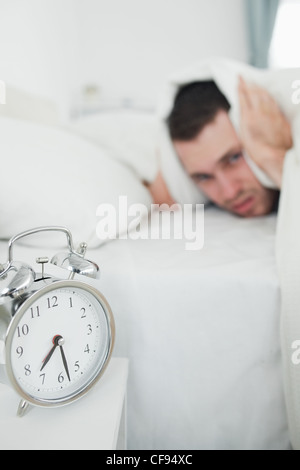 Portrait of a handsome man covering his ears while his alarm clock is ringing Stock Photo