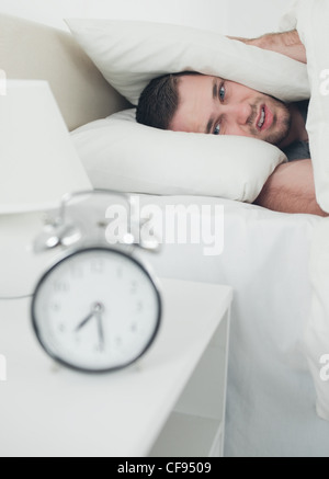 Portrait of a handsome young man covering his ears while his alarm clock is ringing Stock Photo