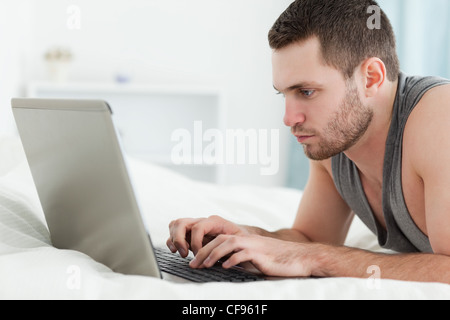 Focused man using a laptop while lying on his belly Stock Photo