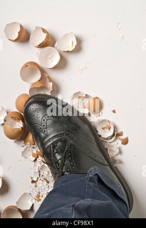 black leather shoe crushing broken eggshells; studio shot on white background Stock Photo