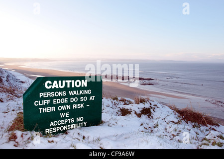 a caution sign on a cliff edge in snow covered ballybunion Stock Photo