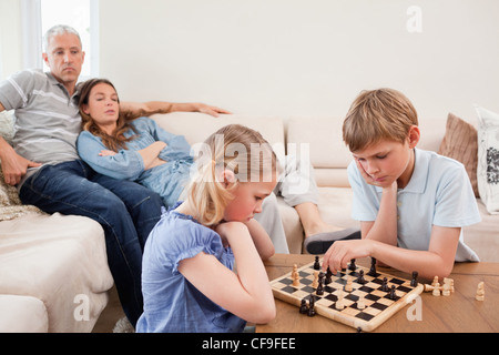 Siblings playing chess in front of their parents Stock Photo