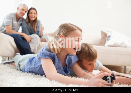Siblings playing video games with their parents on the background Stock Photo
