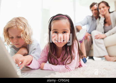 Siblings using a laptop while their parents are in the background Stock Photo