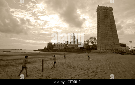 Kids play cricket on beach with Shiva temple in background Stock Photo