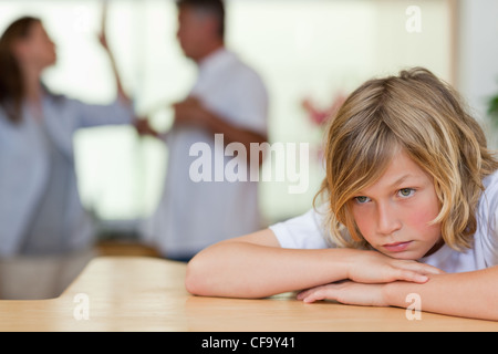 Worried looking boy with fighting parents behind him Stock Photo