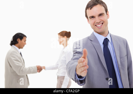 Businessman extending hand with hand shaking colleagues behind him Stock Photo
