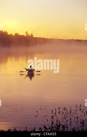 Middle-aged man fly fishing from sea kayak, Lake Muskoka, Ontario, Canada.