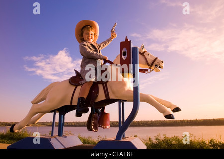 5 year old girl dressed in western attire sitting on amusement pony ride, Canada.