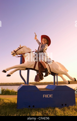 5 year old girl dressed in western attire sitting on amusement pony ride, Canada.