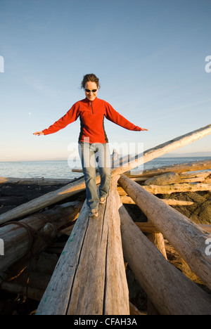 A woman balances on a drift log on the beach near Victoria, Vancouver Island, British Columbia, Canada. Stock Photo